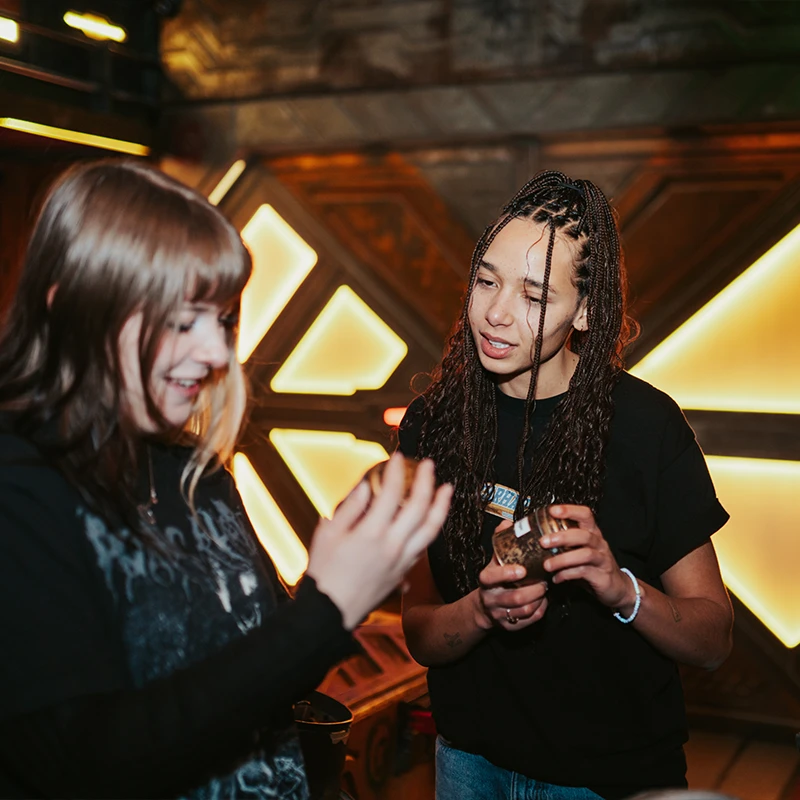 Zwei Studentinnen tauschen sich in einer futuristisch beleuchteten Escape-Room-Kulisse bei Final Escape Berlin aus.